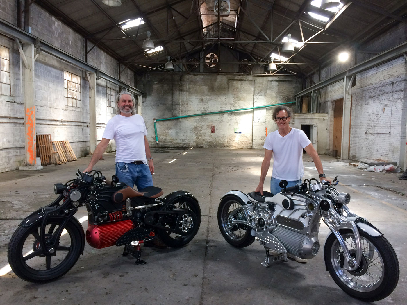 two men with motorcycles in a warehouse